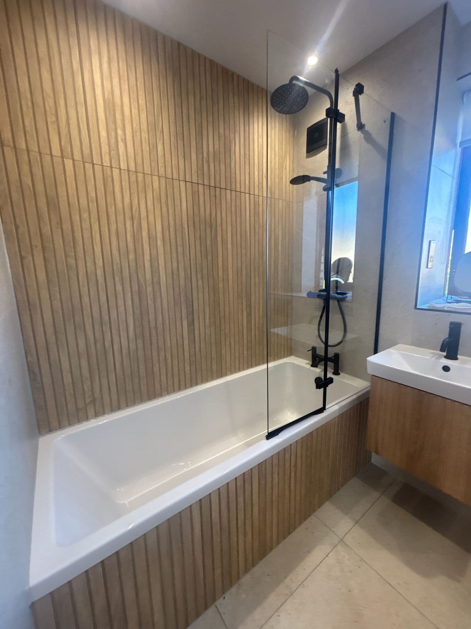Bathroom with a white bath, black shower screen and timber-slatted wall