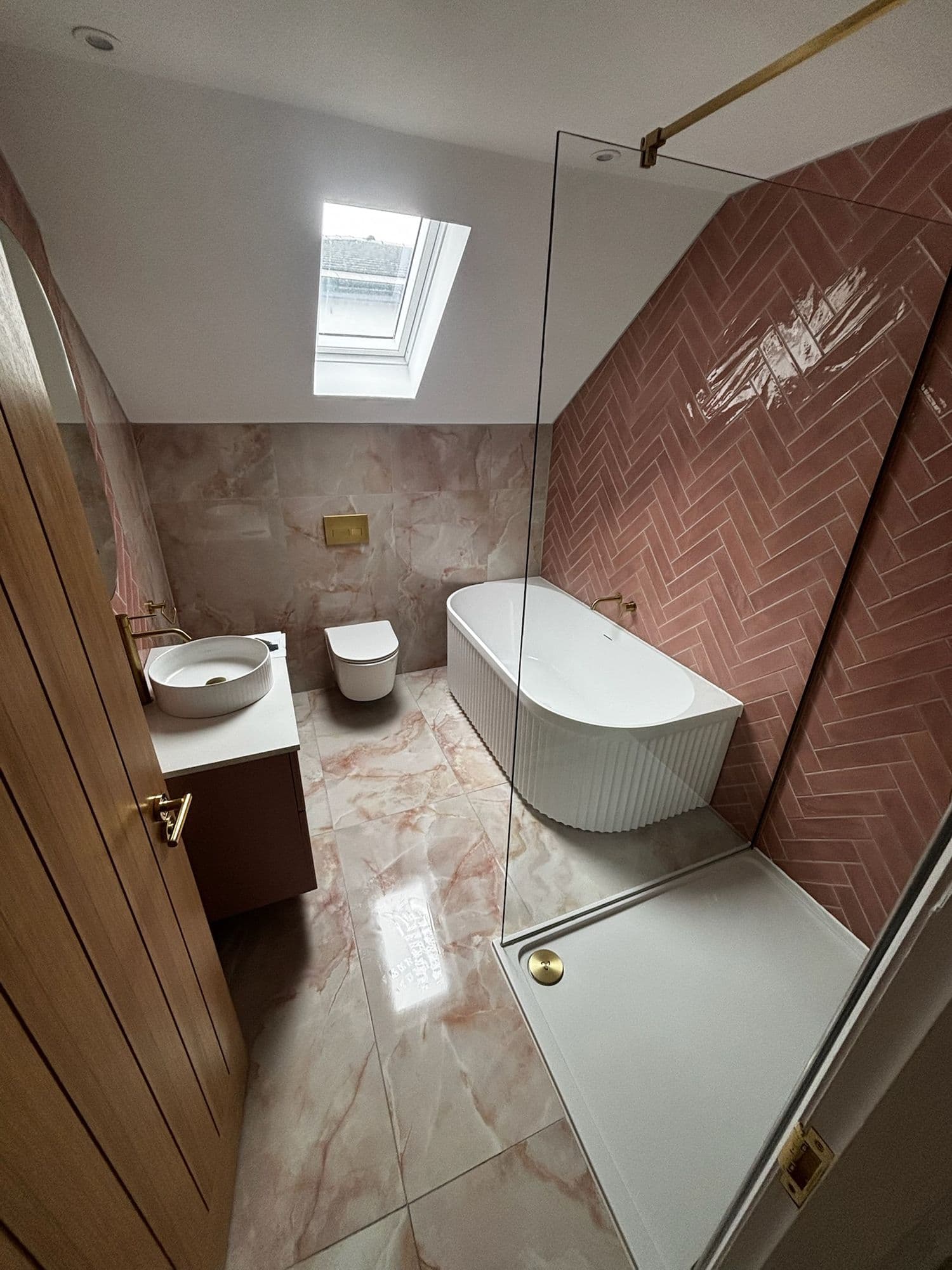 Bathroom with a freestanding bath, herringbone tiled wall and skylight