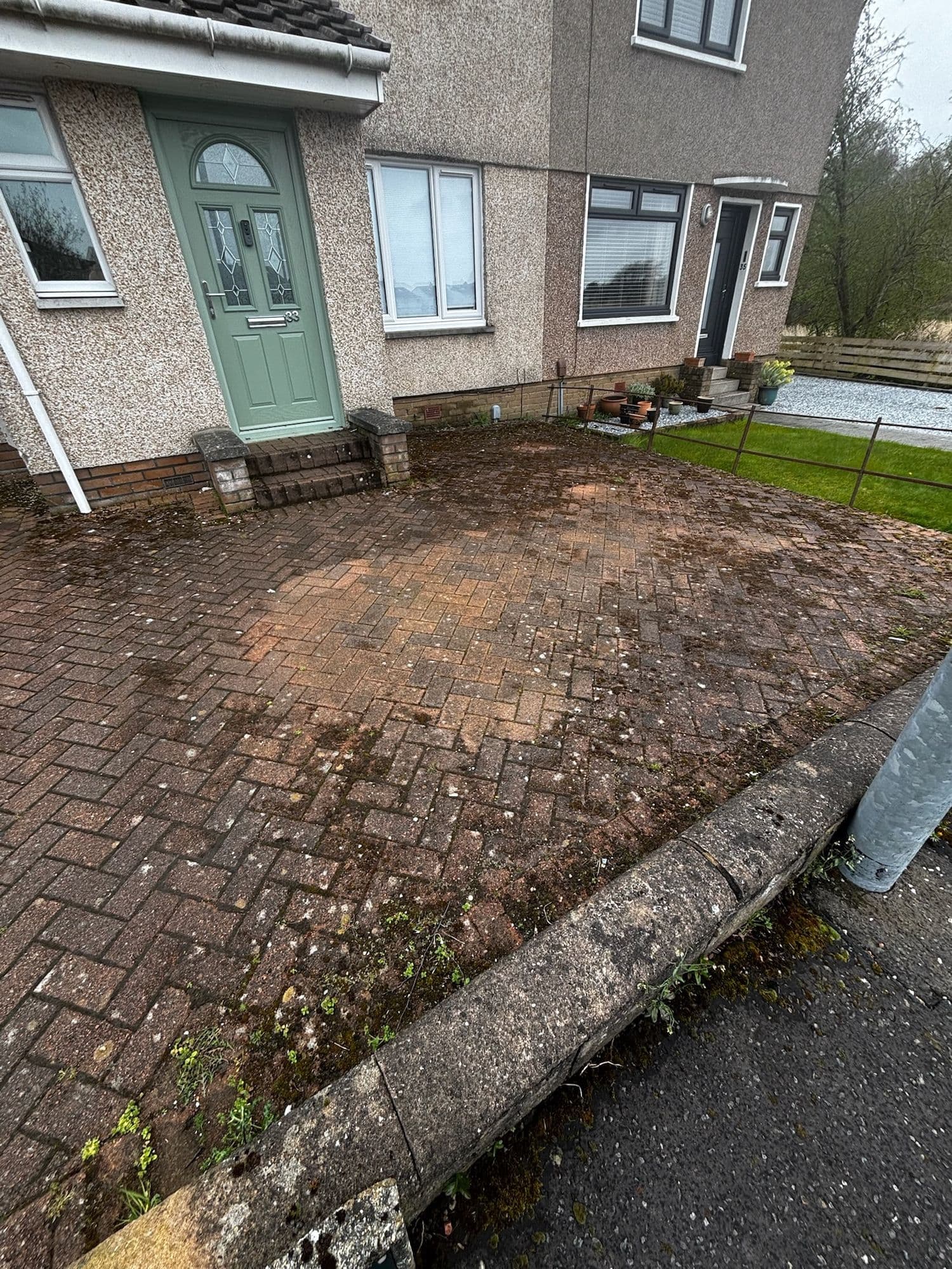 Before: Block paving driveway in front of a semi-detached house, dark with moss and weeds before restoration