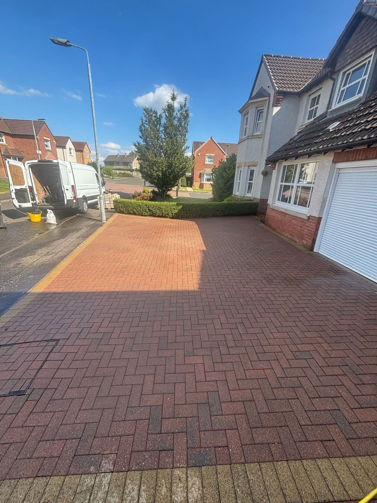 Red block paving driveway after cleaning outside a detached house in sunshine