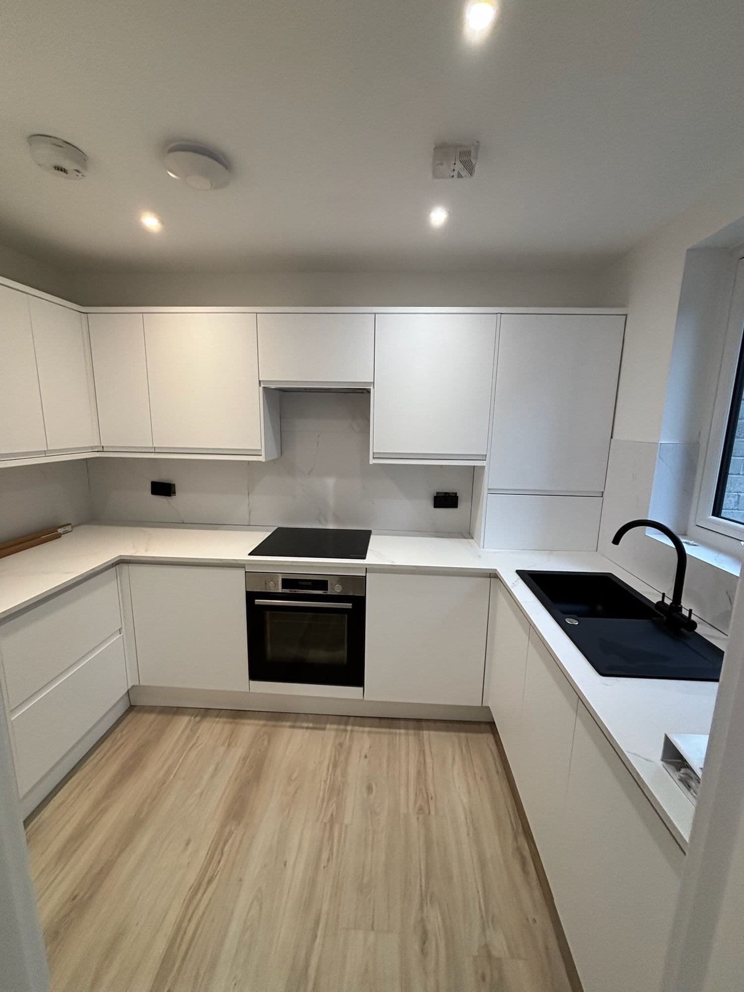 New-build flat kitchen with white handleless units and wood-effect floor