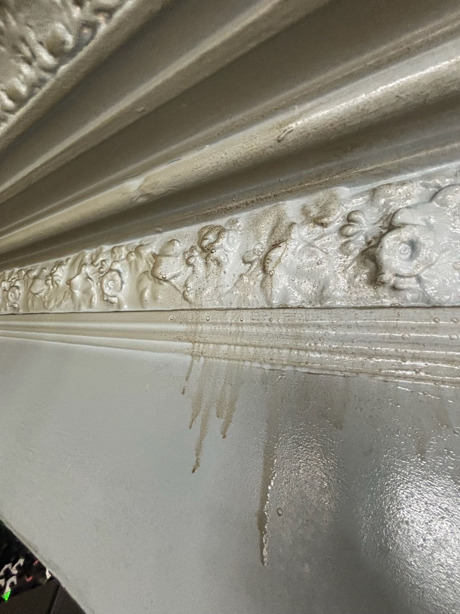 Grease streaks running down a painted surface below an ornate cornice