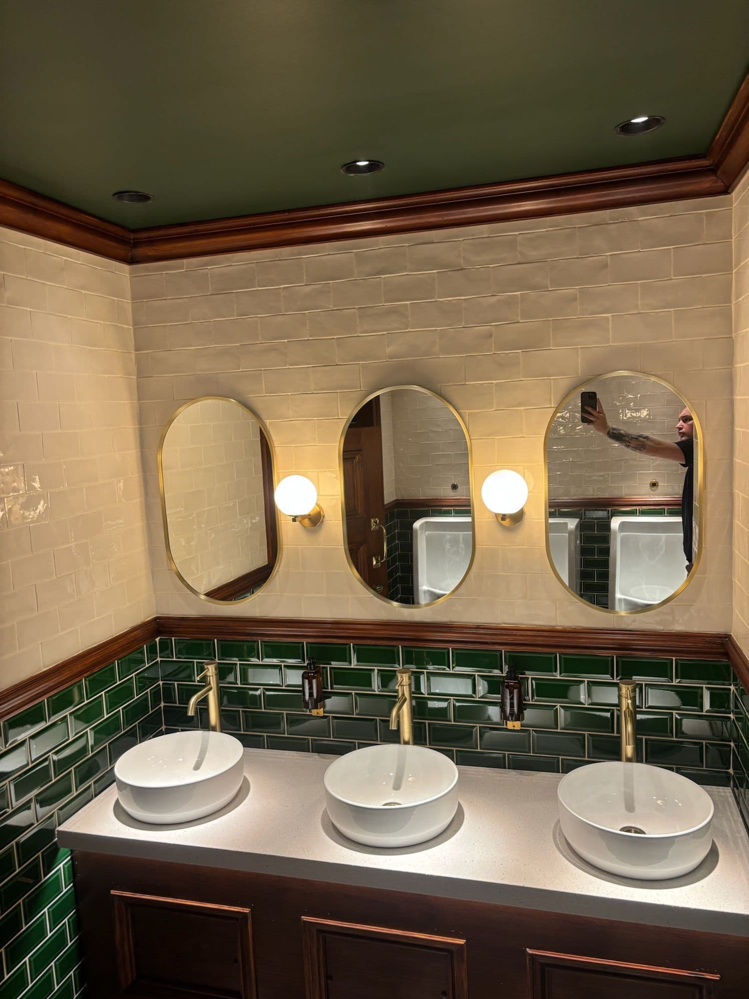 Row of vessel basins with brass taps and oval mirrors in a heritage washroom