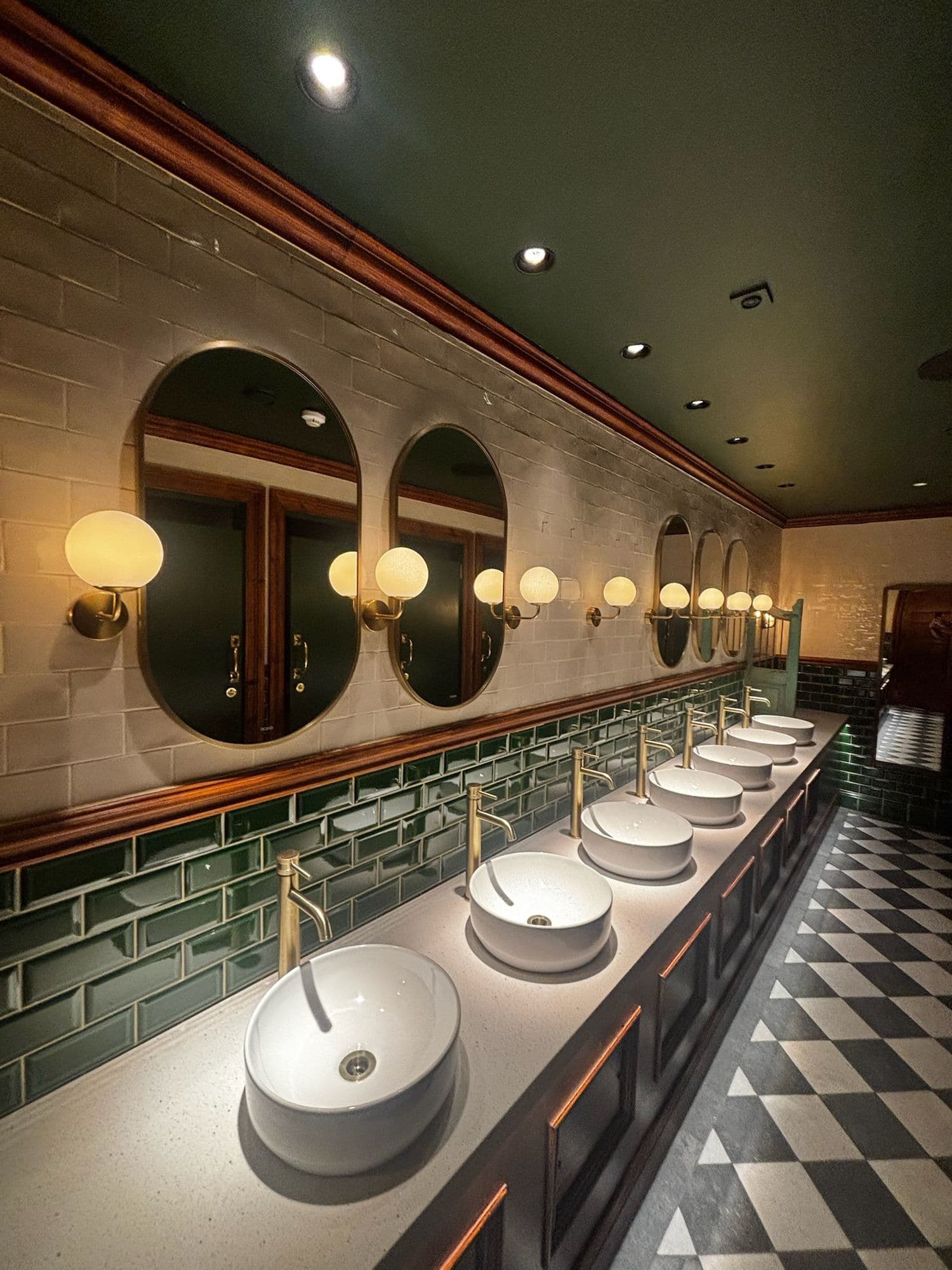 Restored heritage washroom with round mirrors, globe lights, green tiles and chequered floor