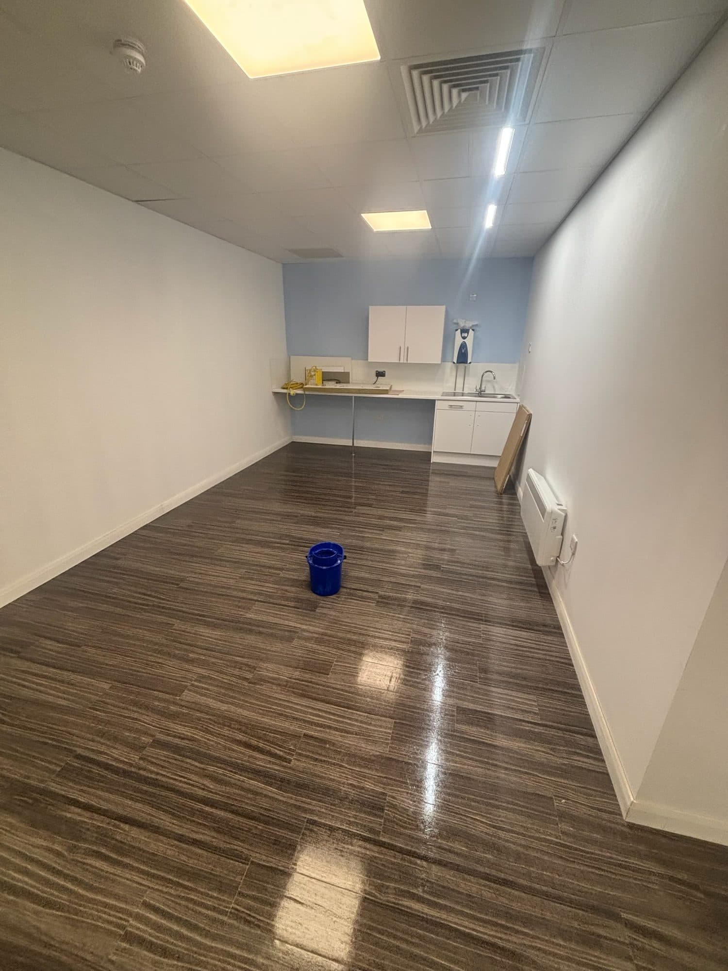 Long empty unit with a polished wood-effect floor and a kitchenette at the far end, ready for a new tenant