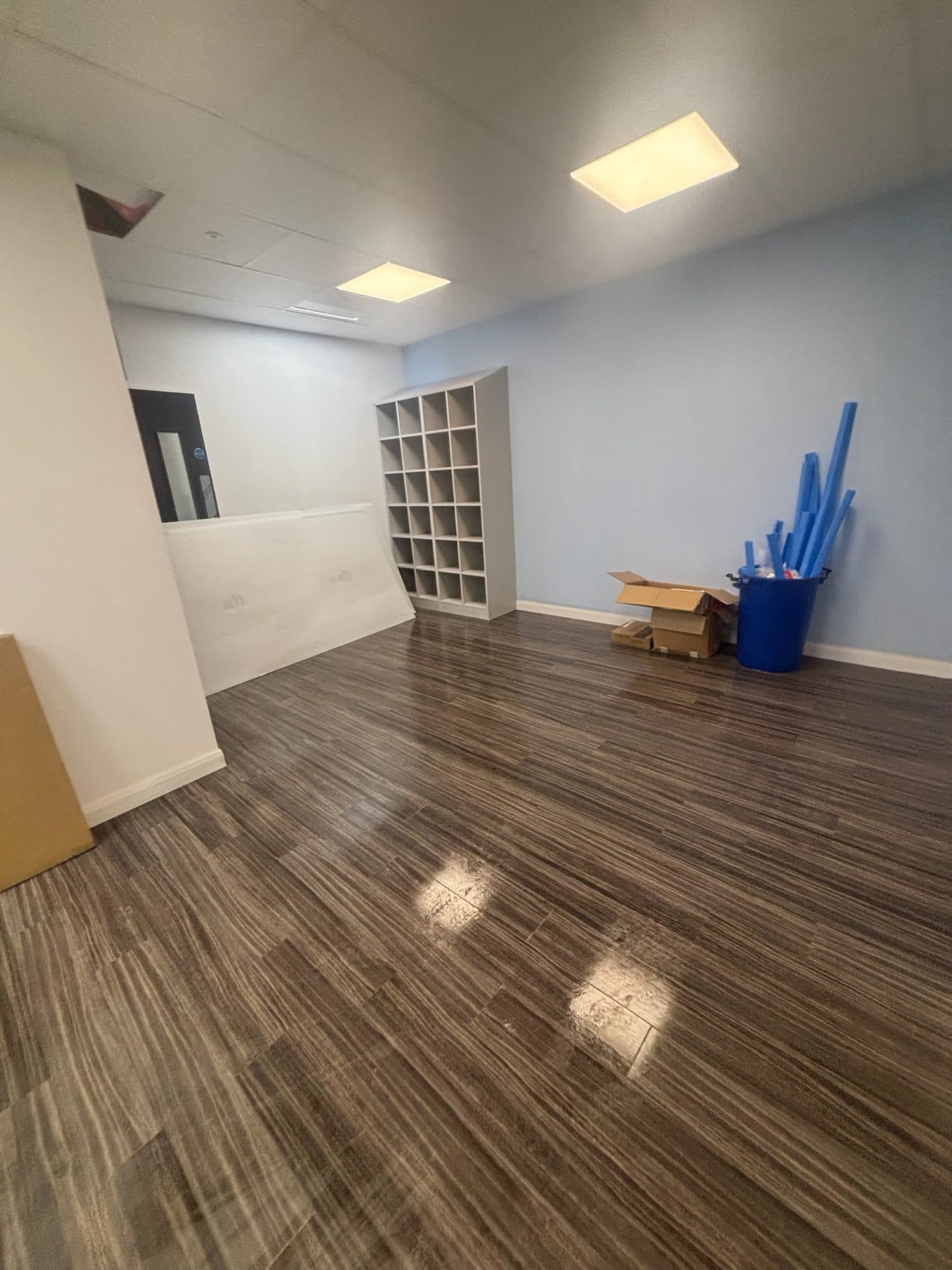 Empty commercial unit with freshly cleaned wood-effect floor, pigeonhole shelving and a pale blue wall