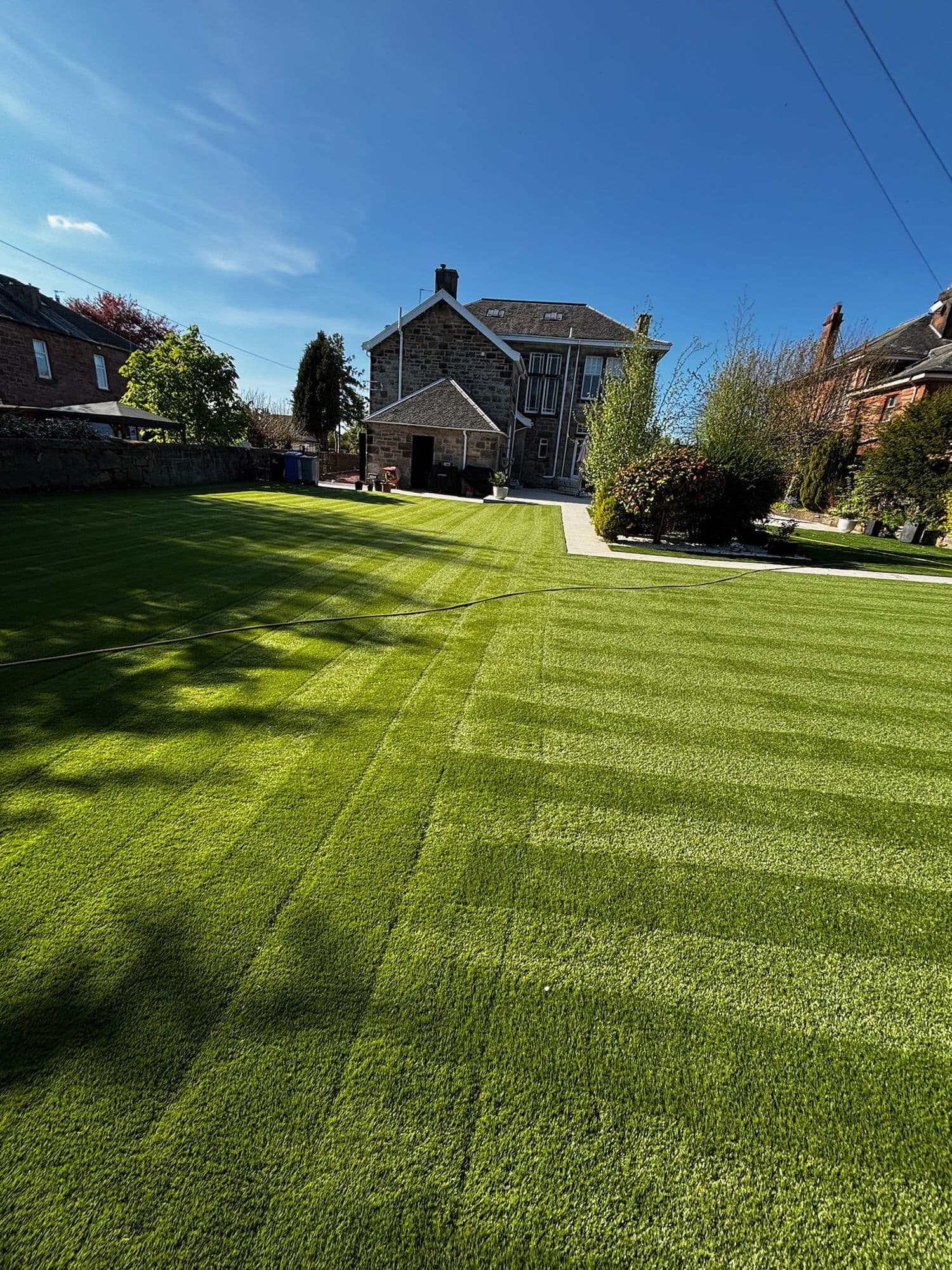 Large striped lawn in front of a stone house and mature trees