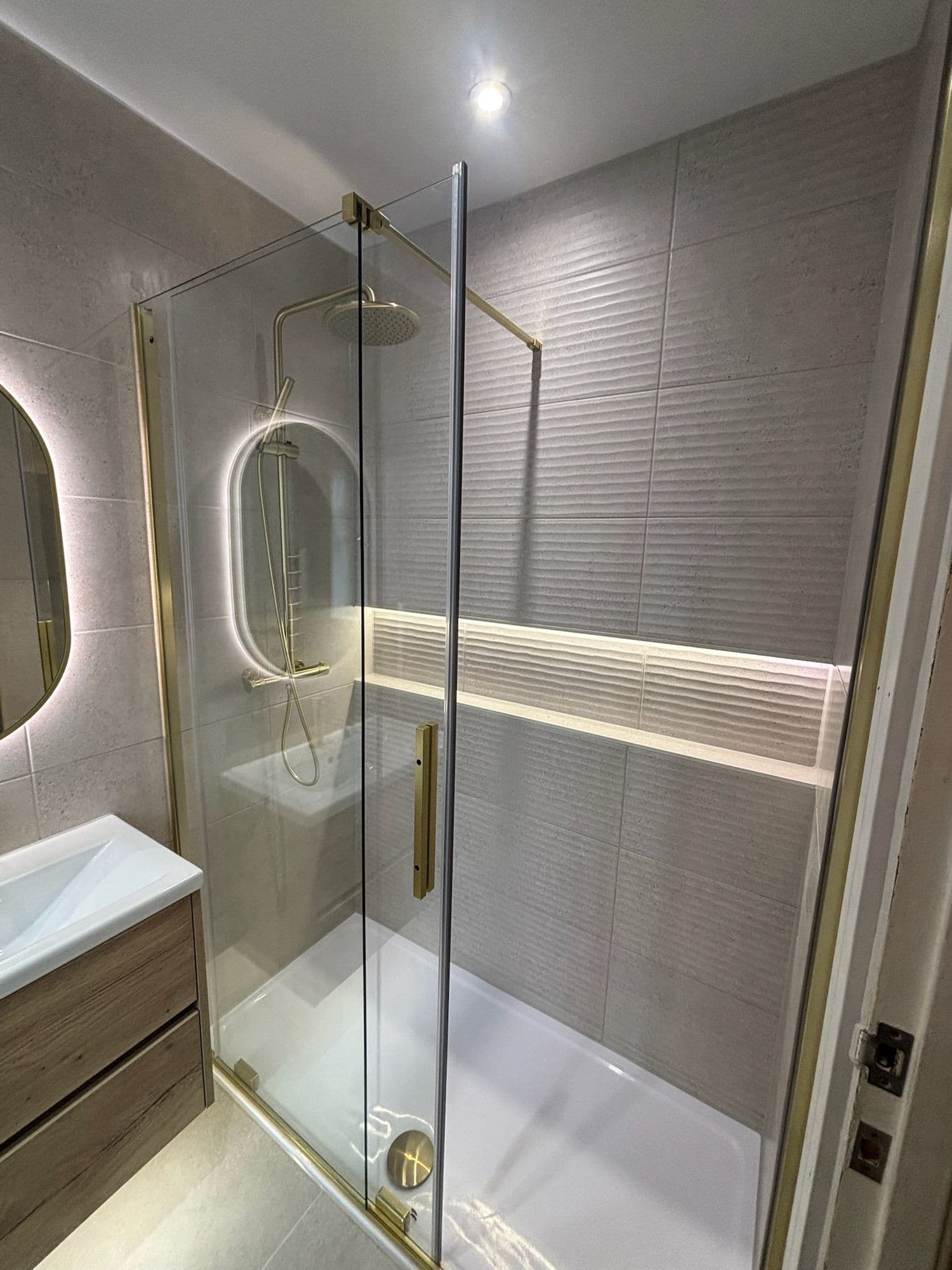 Shower room with a lit oval mirror, brass fittings and glass enclosure