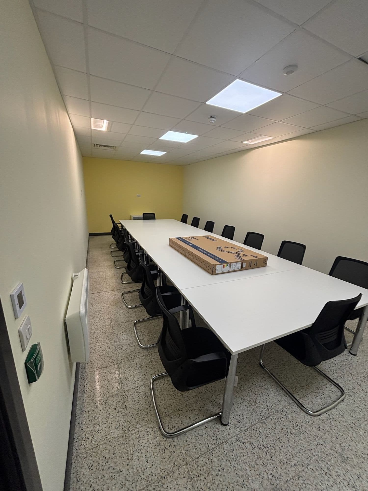 Long meeting table with black chairs in a bright room with a yellow feature wall