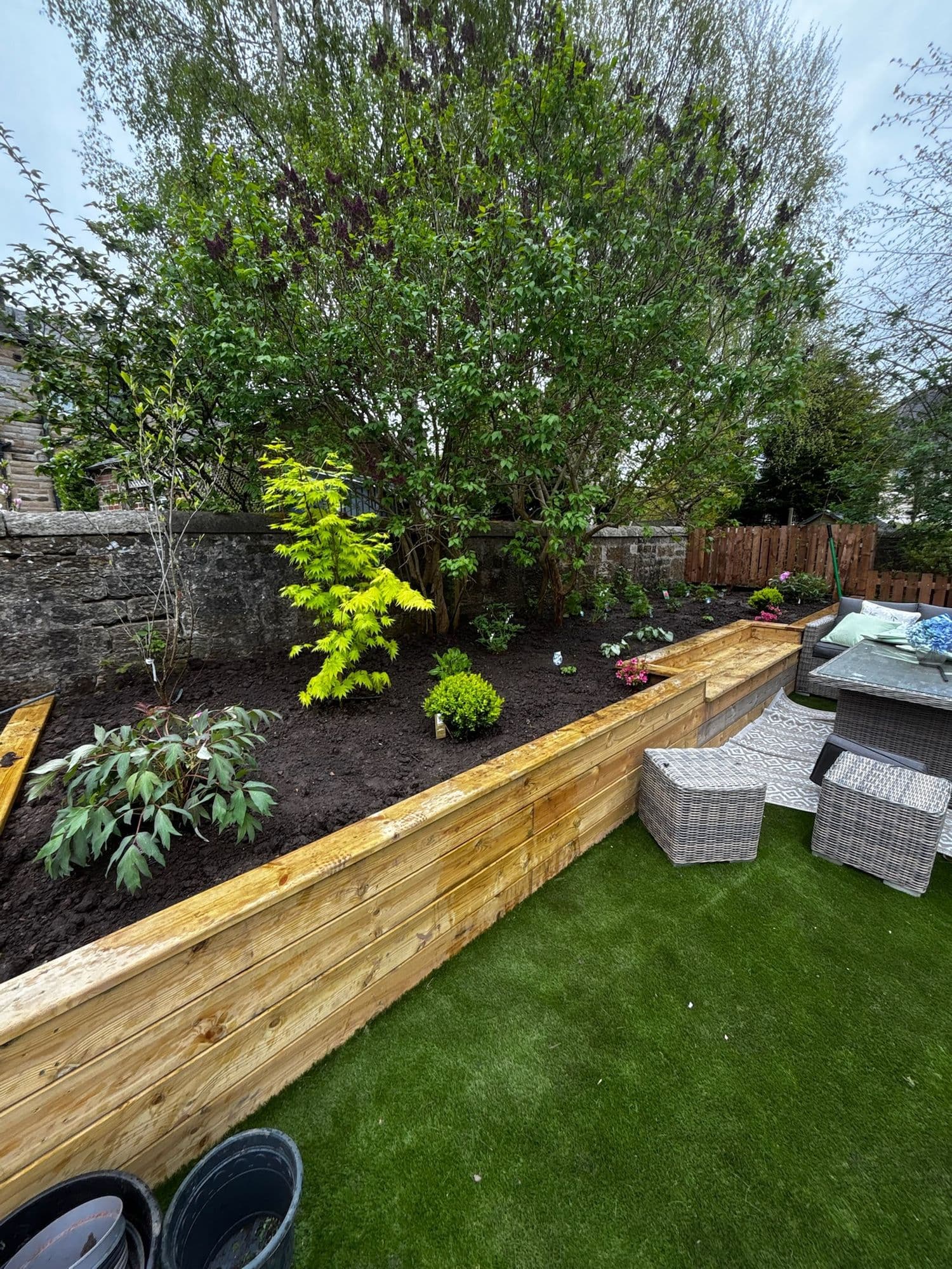 Timber raised beds planted with shrubs beside an artificial lawn