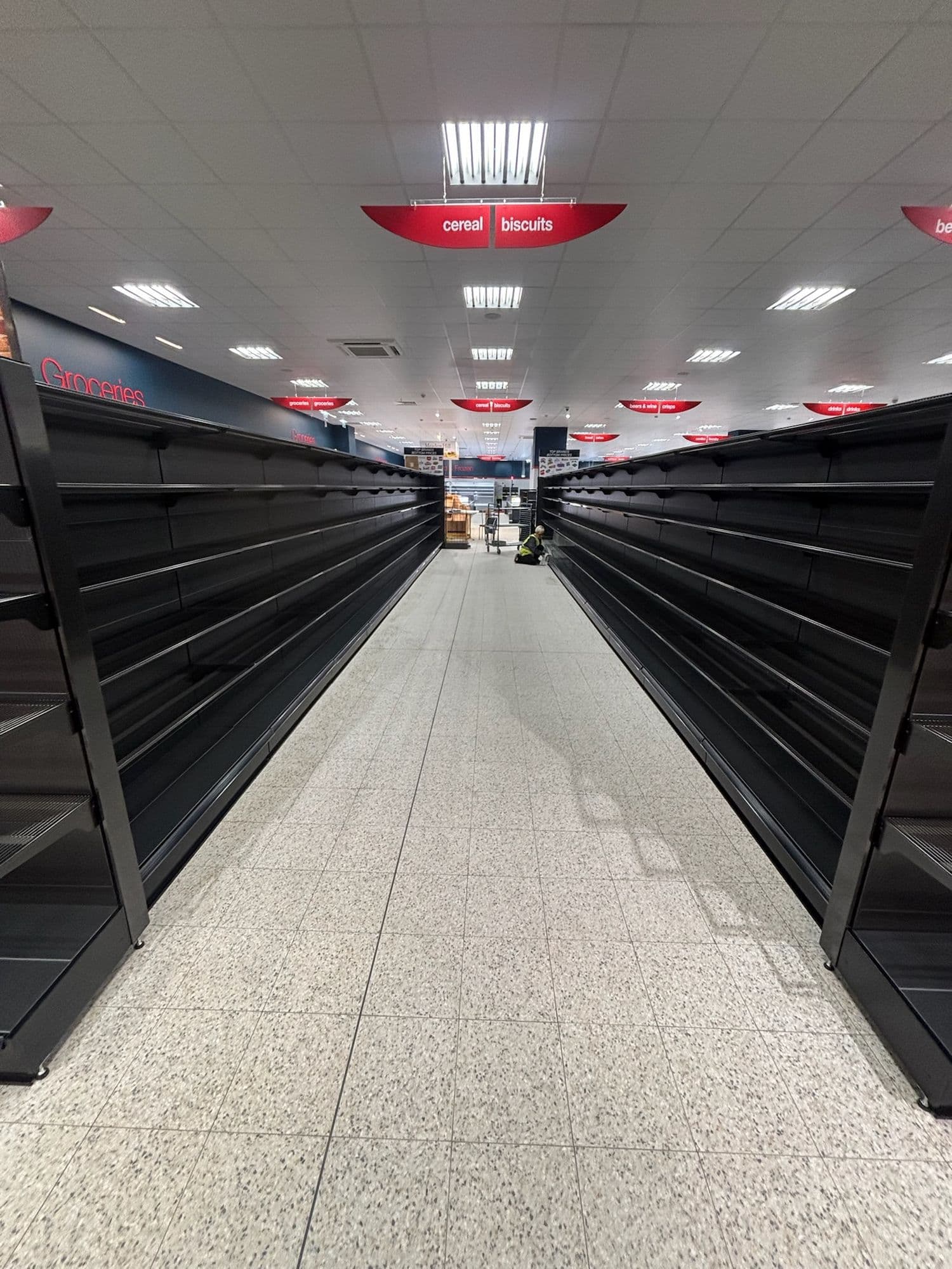 Long store aisle of empty black shelving and a polished floor before opening