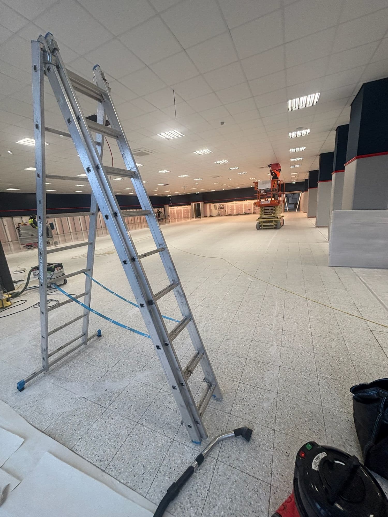 Store fit-out in progress with ladders, vacuum and equipment on a speckled floor
