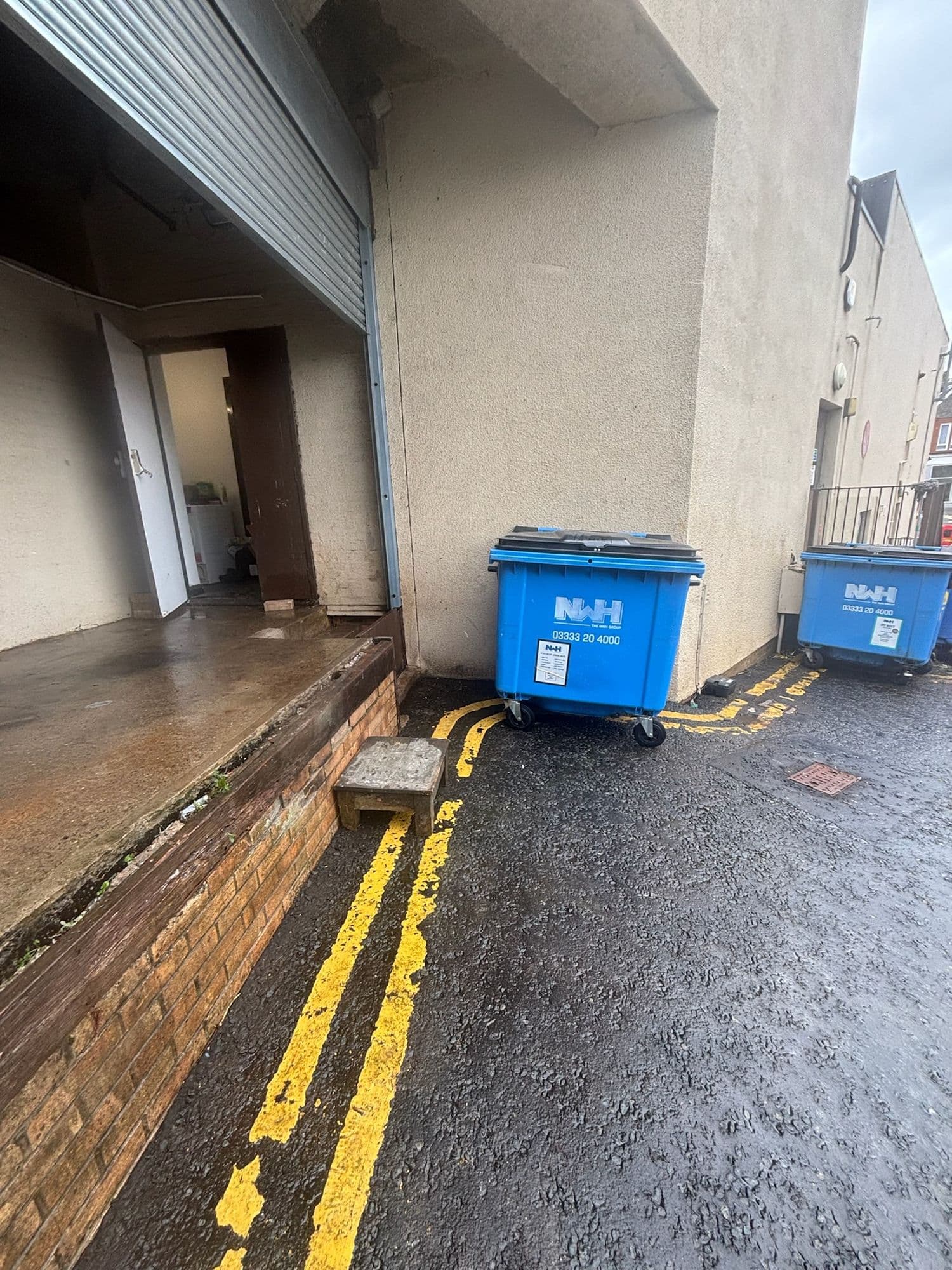 Washed-down service lane with bright yellow lines beside a loading door and bins