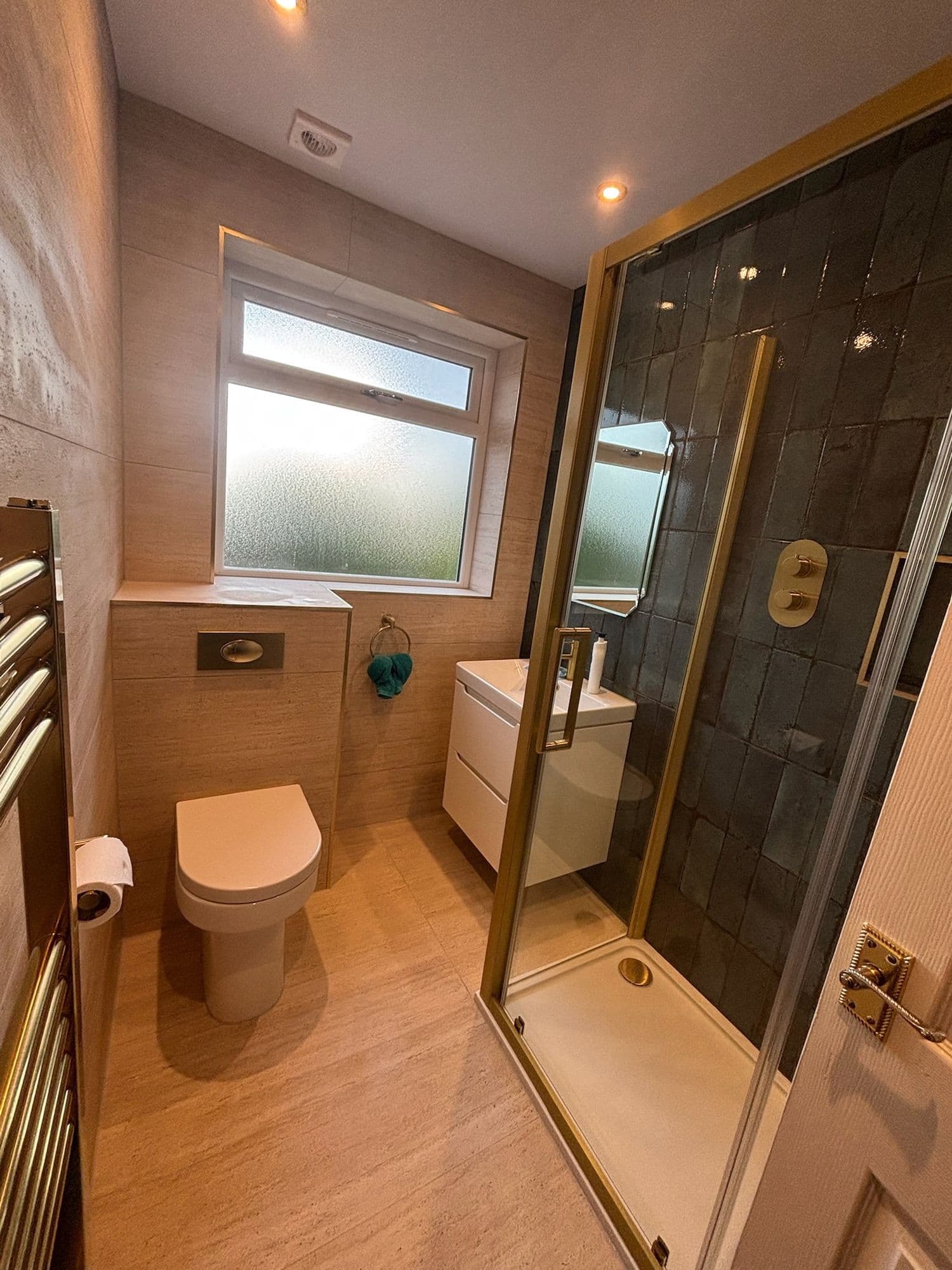 Shower room with dark tiled enclosure, brass fittings and a frosted window