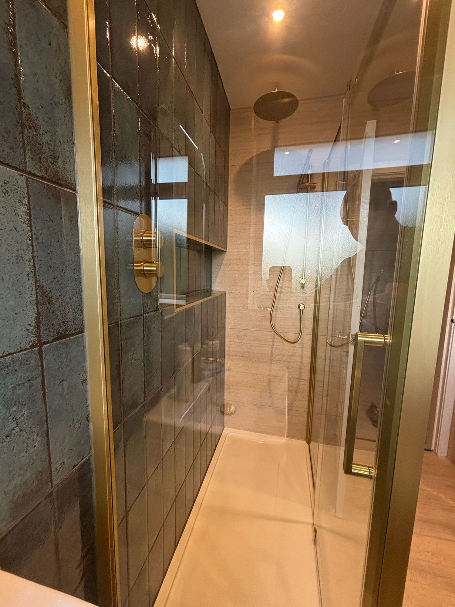 Walk-in shower with dark green tiles, brass frame and rainfall head