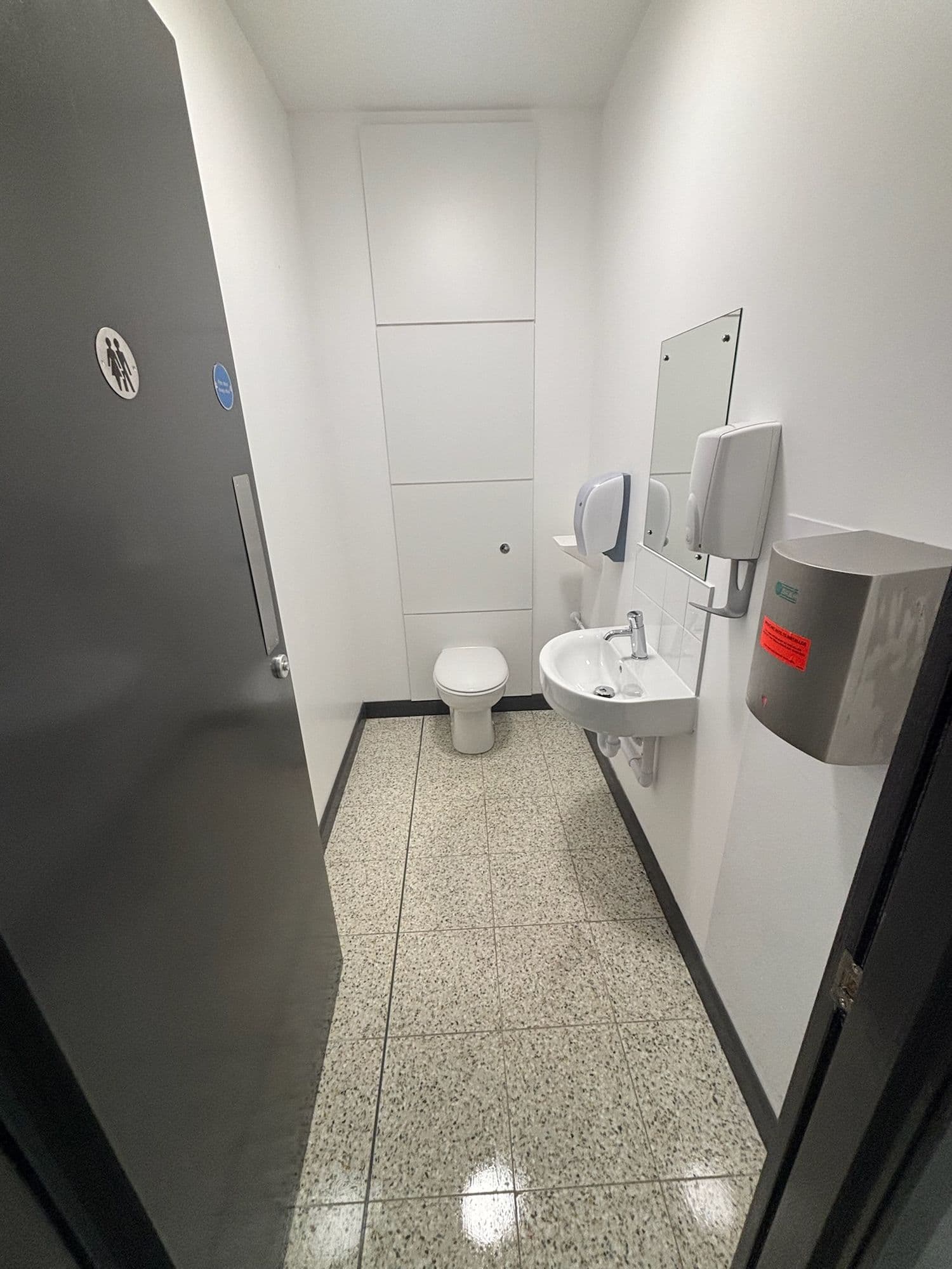 Washroom cubicle with dark door, white walls and polished speckled floor