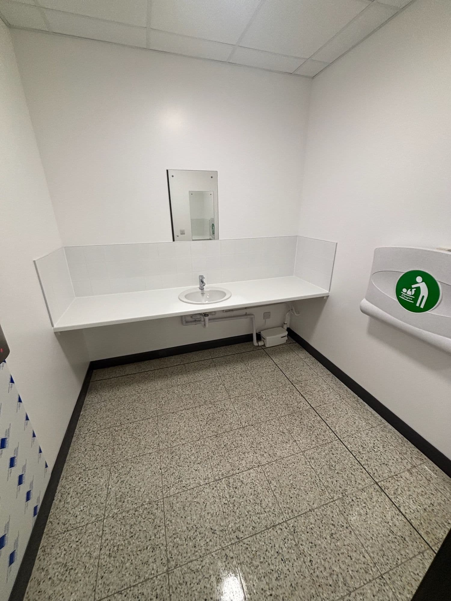 Washroom with a long white vanity counter, mirror and baby change unit